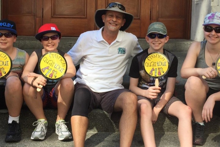 Group of five sitting on steps, holding paddles saying 'French Quartour Kids' and smiling.