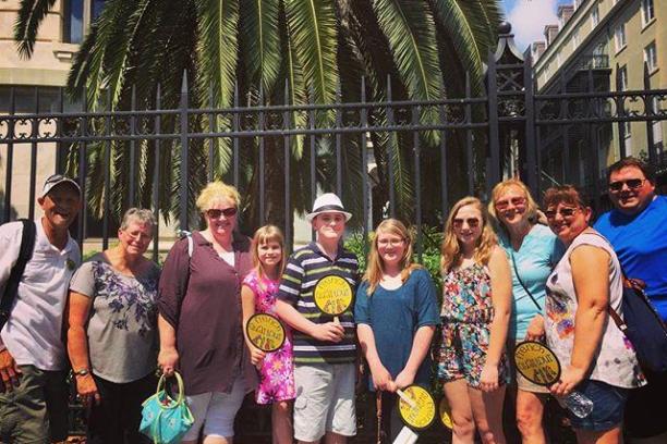 Group of people posing in front of a wrought iron gate and palm tree on a sunny day.