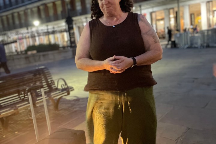 Person standing near a lit lantern on a city street at dusk.