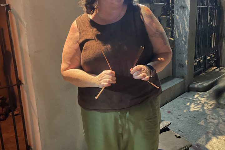 Person holding sticks, standing on a sidewalk at night.