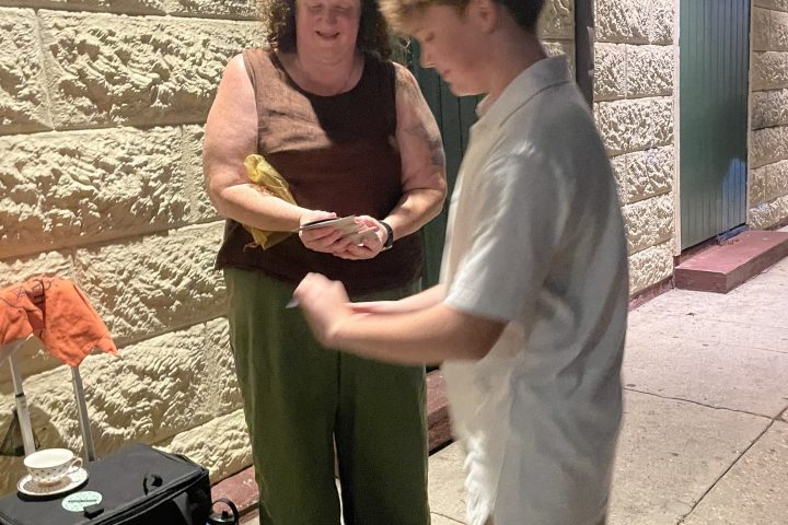 Two people standing near a wall, one holding an item, with a bag on the ground.