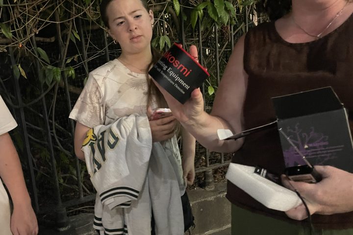 People smiling, one holding a black box, standing outside on a sidewalk.